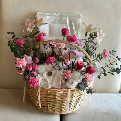 Pink flower bouquet in Sweet Beginnings Basket featuring baby essentials for newborn gift